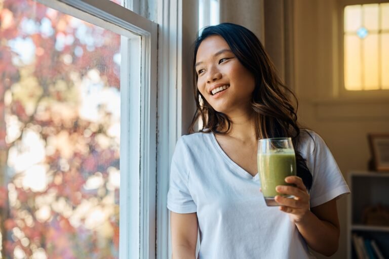 Happy Asian woman drinking fresh smoothie while looking through the window.