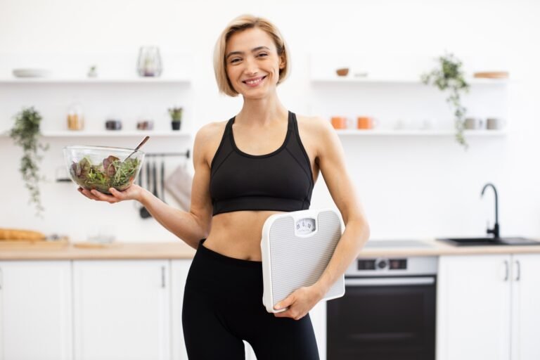 Healthy woman holding salad bowl and weighing scale in kitchen